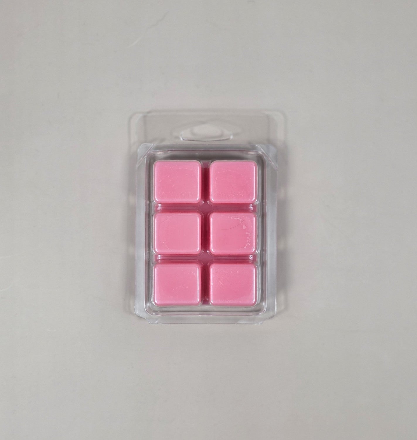 Pack of pink wax melts in a clear plastic packaging on a light gray background