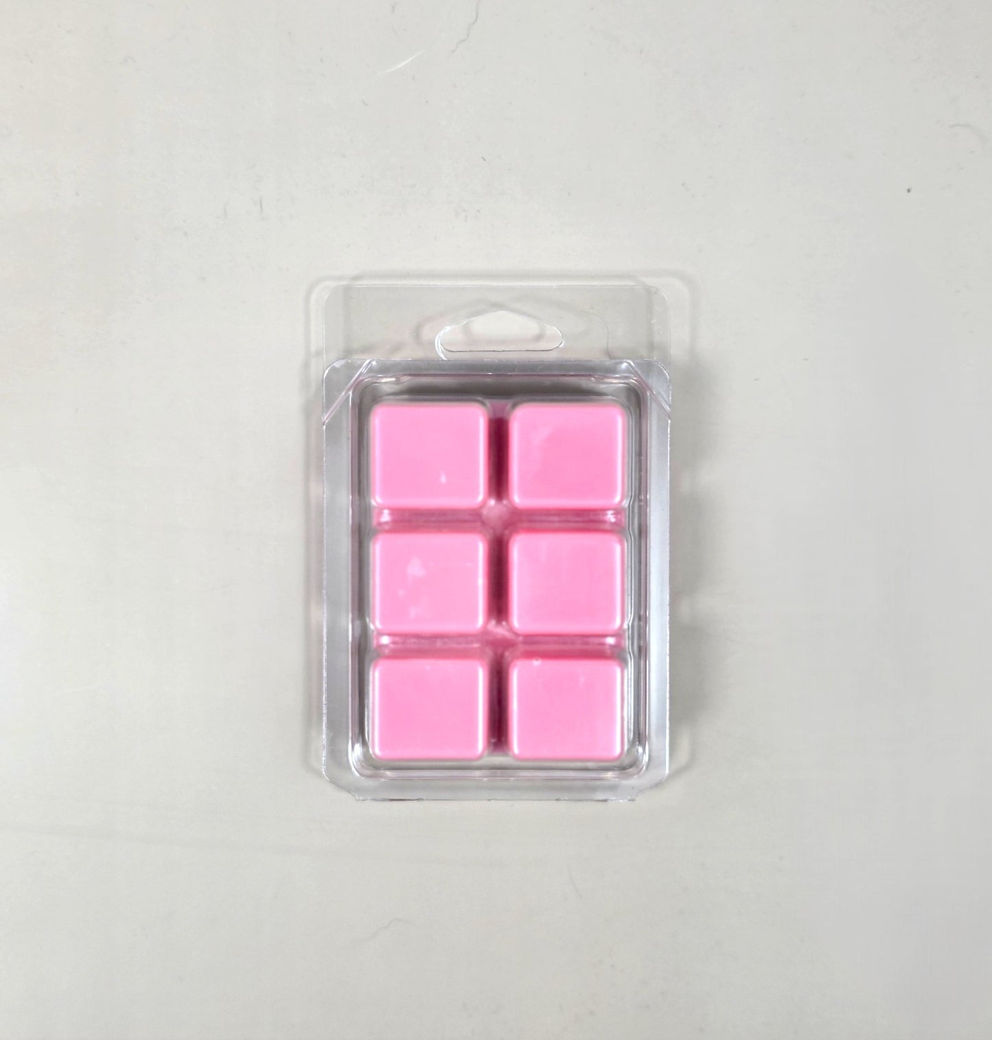 Underside view of a clear plastic 6-cube clamshell package showcasing vibrant pink soy wax melt cubes.