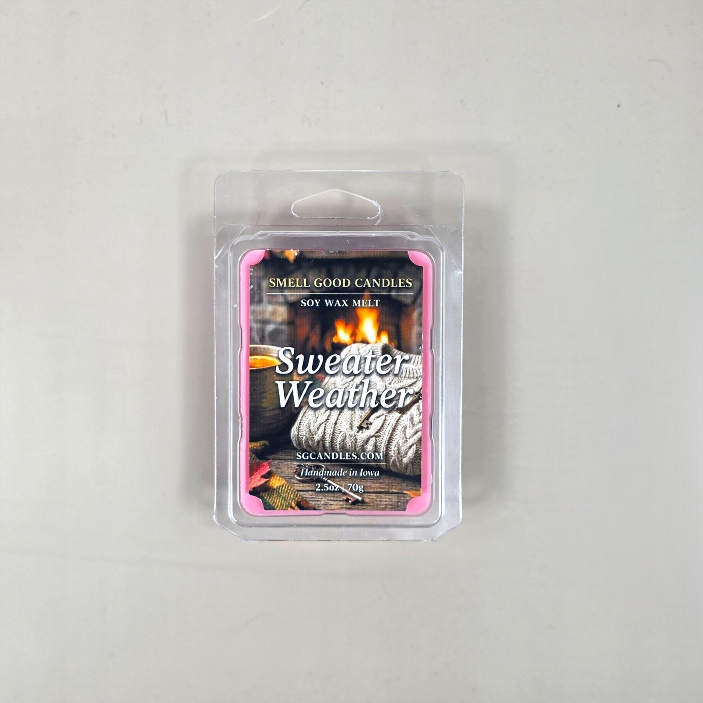 Top view of Sweater Weather fragrance soy wax melt in a 2.5oz clear clamshell package featuring a cozy label design with a knit sweater, a warm mug, and a roaring fireplace.