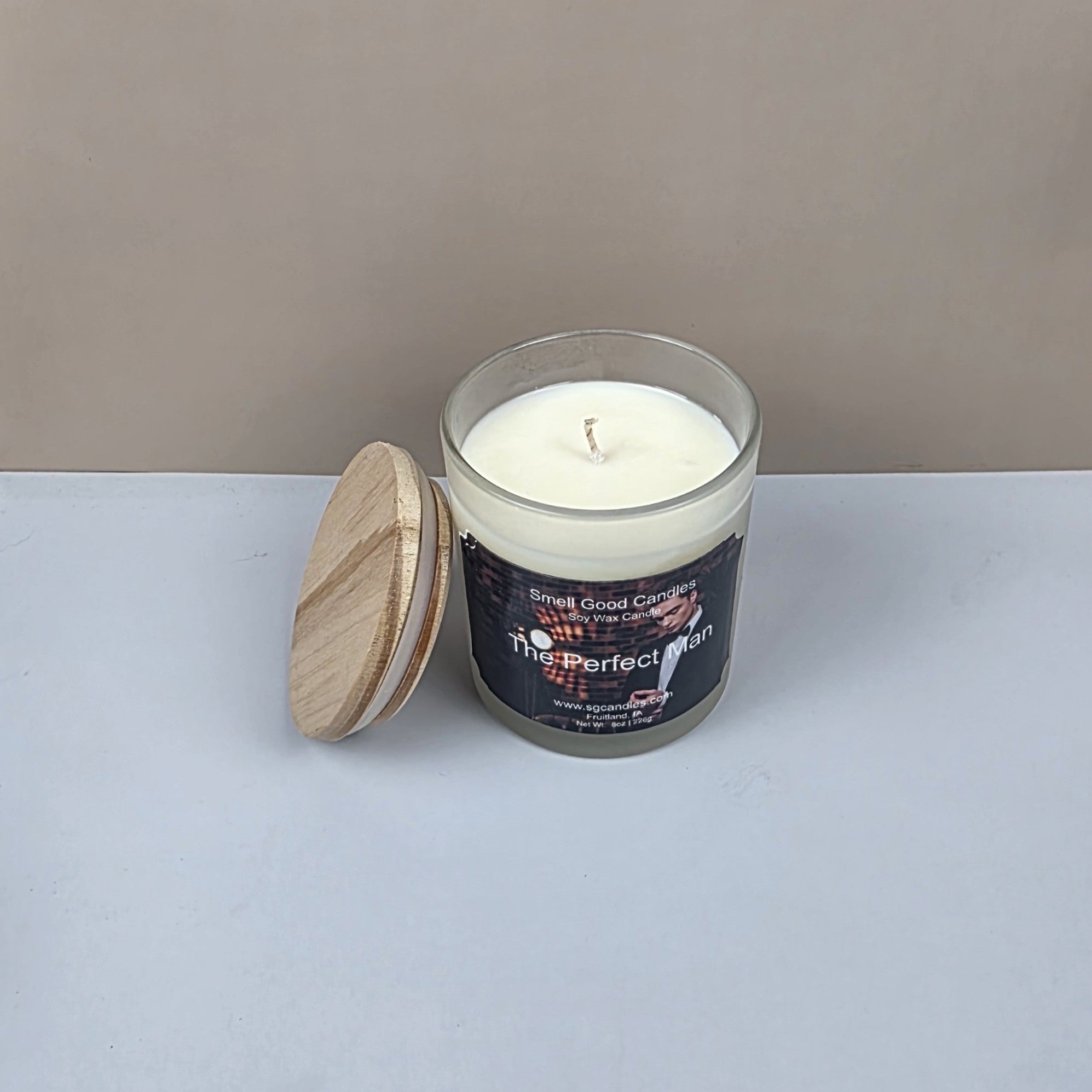Candle in a glass jar with a wooden lid on a white surface against a beige background