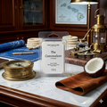 The Commodore Luxe Aquatic wax melt by Smell Good Candles, featuring scent notes of Mahogany, Coconut, Aquatic, Herbal, and Suede, on a white marble and dark wood desk with a vintage brass compass.