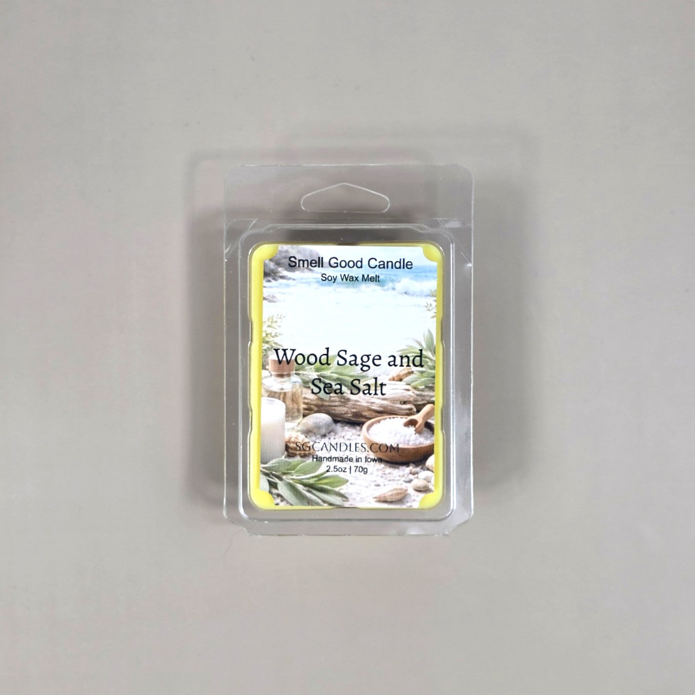 Labeled Wood Sage & Sea Salt soy wax melt in a 2.5oz clamshell featuring a peaceful coastal scene with driftwood and ocean waves.